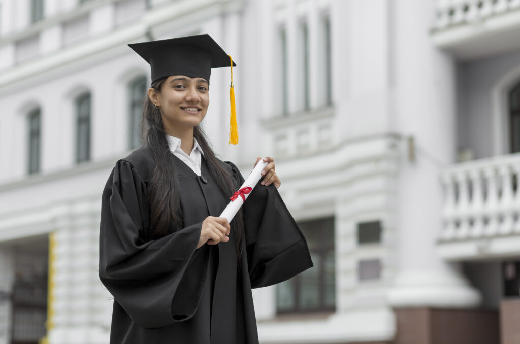 Young female wearing graduate uniform holding her degree in front of university campus