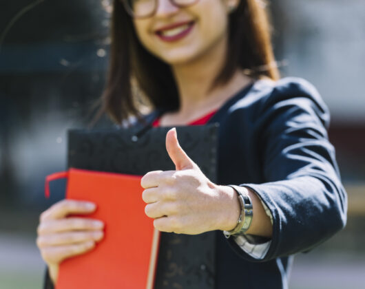 Young girl doing thumbs up holding books