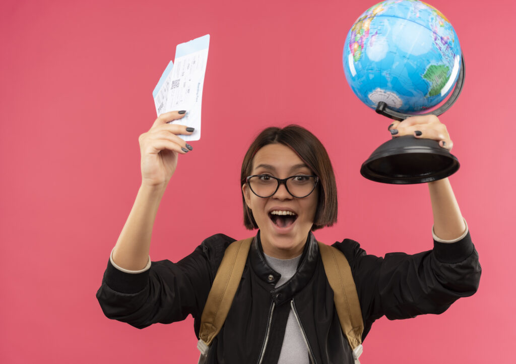 Young happy student waering glasses, holding globe in one hand and aeroplane tickets in another hand
