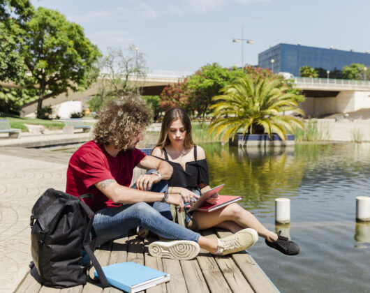Students studying near lake carrying books and bags