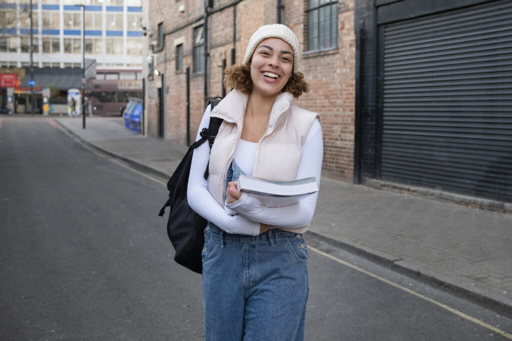 Smiley female student standing on street holding books and bag
