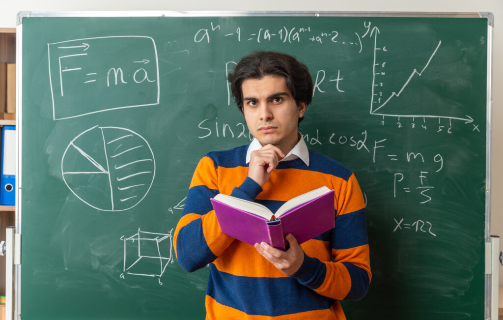 young man holding book standing in front of green board