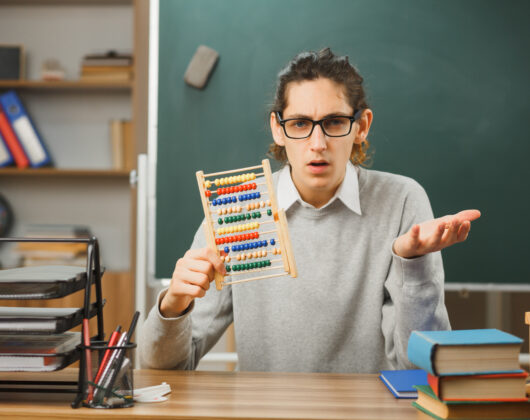 a young male teacher sitting and holding abacus in a classroom