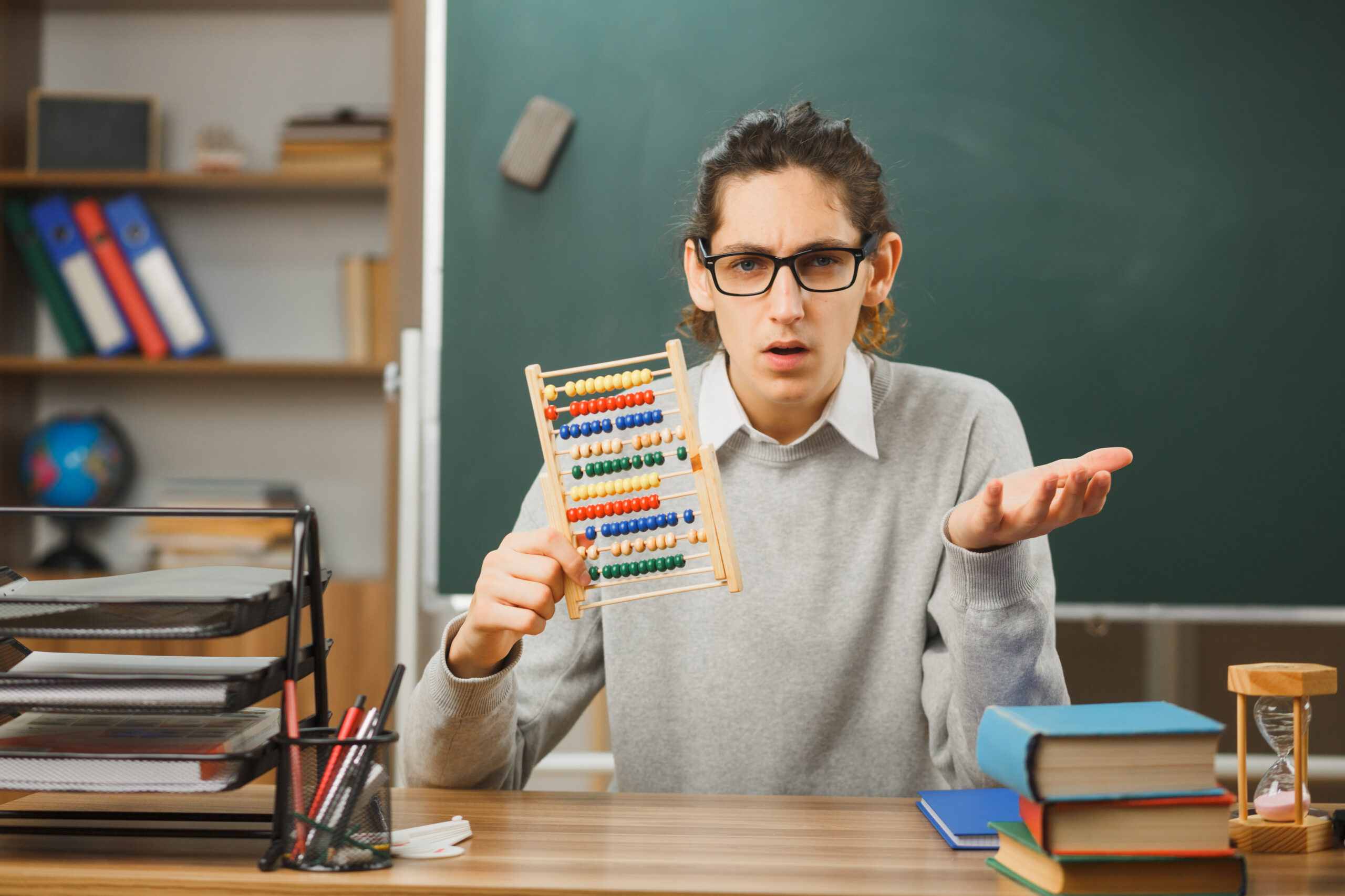 a young male teacher sitting and holding abacus in a classroom